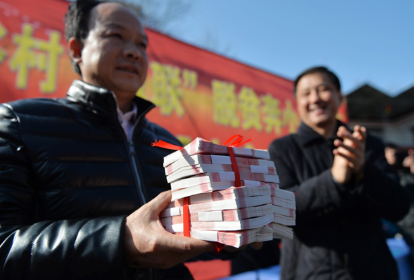 甘肃省陇南市康县城关镇凤凰谷村首次“村民分红扩股”大会上，一名村民代表上台领取股东年度分红（2015年12月25日摄）。入股村民分别拿到三千至五万元不等的年度分红和精准扶贫奖励。据了解，2014年以来，贫困村凤凰谷村在陇南市“双联”扶贫单位帮助下，启动了一项“股份制”脱贫试验。利用当地乡村特色旅游资源开办乡村旅游度假公司，大力发展农家客栈、有机果蔬种植和乡村体验旅游。村集体和13户村民入股成为公司股东，“双联”单位和村集体还帮助19户贫困户垫资3000元参股，总融资35万元的股份制公司在运营近一年后营业额突破100万元，实现利润46万元，股东和参股贫困户按照1:1的比例分红。2015年凤凰谷村人均收入8000元以上，比四年前翻了两番，实现了整村脱贫。