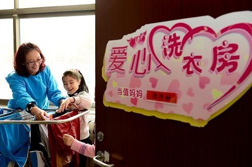 3月10日,在威海市经济技术开发区新都小学,爱心洗衣房“当值妈妈”梁玲丽和留守儿童一起晾晒衣服。为解决留守儿童生活中的一些实际困难,山东省威海市经济技术开发区新都小学在校园里建立了“爱心洗衣房”,每周“当值妈妈”收集并清洗留守儿童的衣物,将关爱落到行动中。新华社记者 郭绪雷 摄 3月10日,在威海市经济技术开发区新都小学,爱心洗衣房“当值妈妈”梁玲丽在