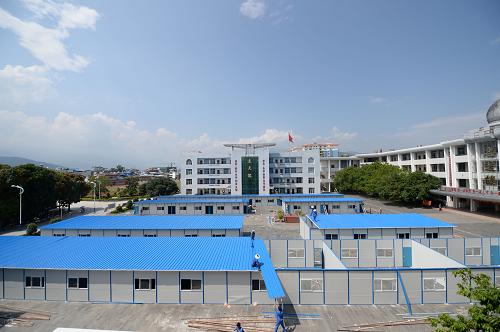 6月2日,施工人员在盈江县第一中学搭建板房考场。高考临近,在云南盈江地震灾区,用作高考考场的板房正在紧张搭建,全县1000余名考生届时将在板房中参加高考。据介绍,由于灾区夏季气温高,板房考场采取了降温防暑措施,板房完工后外层要架设一层防晒网。当地教育部门还联系了制冰企业,高考时将在板房内使用冰块降温。新华社发(胡超 摄)