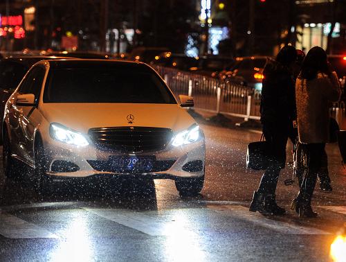 1月24日,几名行人在北京东三环附近一处斑马线等候过马路,细小的雪花在其身后的车灯照射下清晰可见。