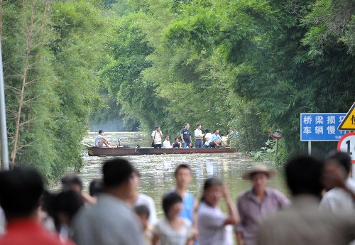 6月14日,在广西梧州市长洲区倒水镇,人们乘船从被水淹没的公路上通过。新华社记者 周华 摄