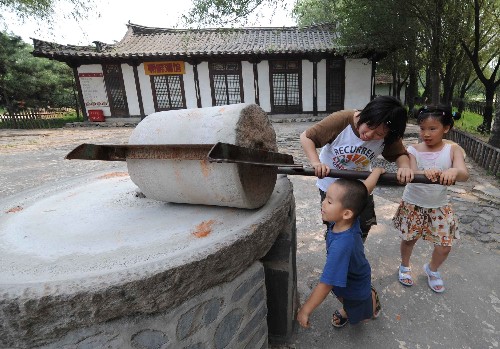 7月26日,三名儿童在北京中华民族园的朝鲜族景区体验朝鲜族石磨。新华社记者 武巍 摄