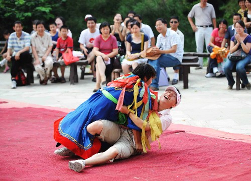 7月26日,在北京中华民族园的蒙古族景区,游客(下)与蒙古族工作人员表演摔跤。新华社记者 武巍 摄