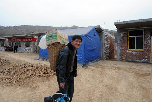 1月22日,陇南康县豆坪乡豆坪村一位村民背着年货行走在新建的房屋前。 新华社记者 金良快 摄